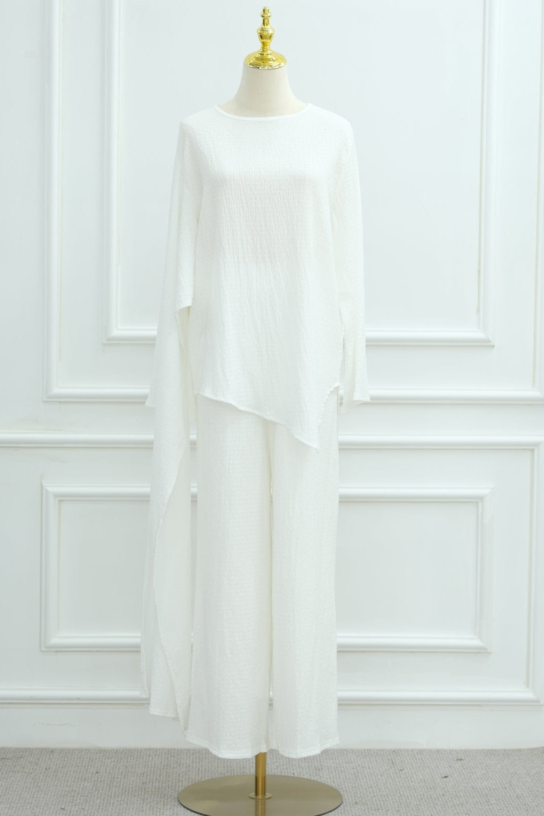 White blouse on a mannequin against a white paneled wall with a plant in the corner.