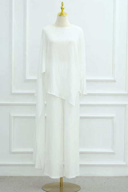 White blouse on a mannequin against a white paneled wall with a plant in the corner.